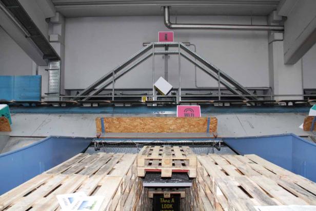 Ein Stapel Holzpaletten in einer Lagerhalle mit Hinweisschildern.