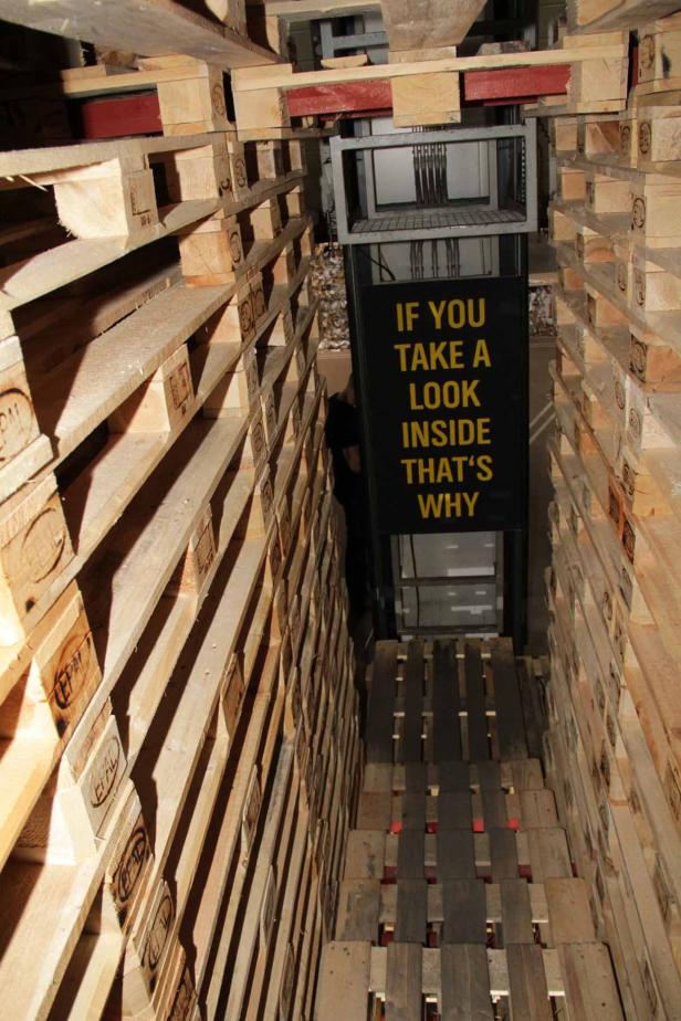 Ein Gang, der vollständig aus Holzpaletten gebaut wurde, mit einem Schild mit gelber Schrift.