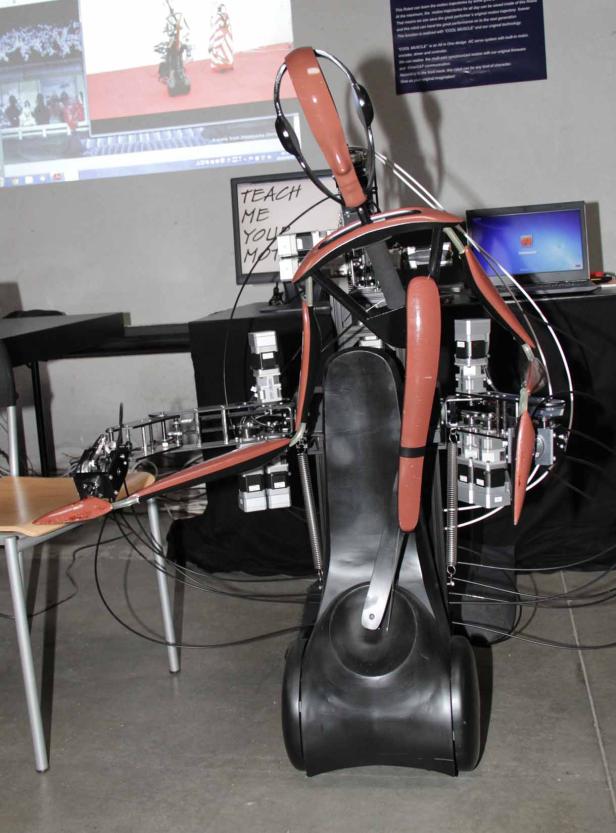 Ein humanoider Roboter mit Kopfhörern steht in einem Raum mit Computern und Kabeln.