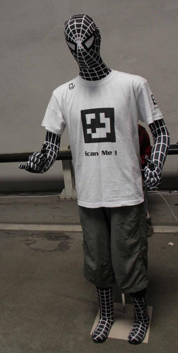 Eine Person in einem Spider-Man-Kostüm mit einem T-Shirt mit der Aufschrift „Scan Me!“.