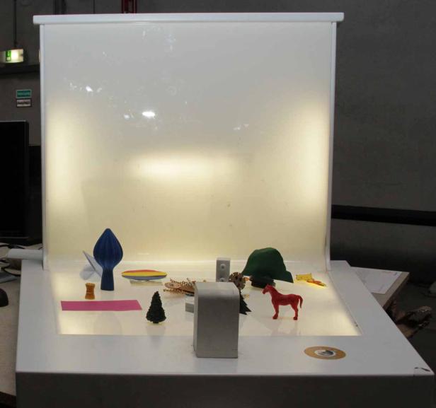 Verschiedene Miniaturfiguren und -objekte sind in einer kleinen Studio-Umgebung angeordnet.