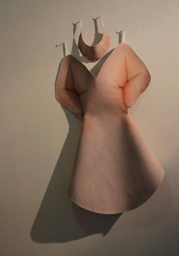 Eine Papierinstallation in Form eines Kleides und eines Halsbandes, die an einer Wand hängen.