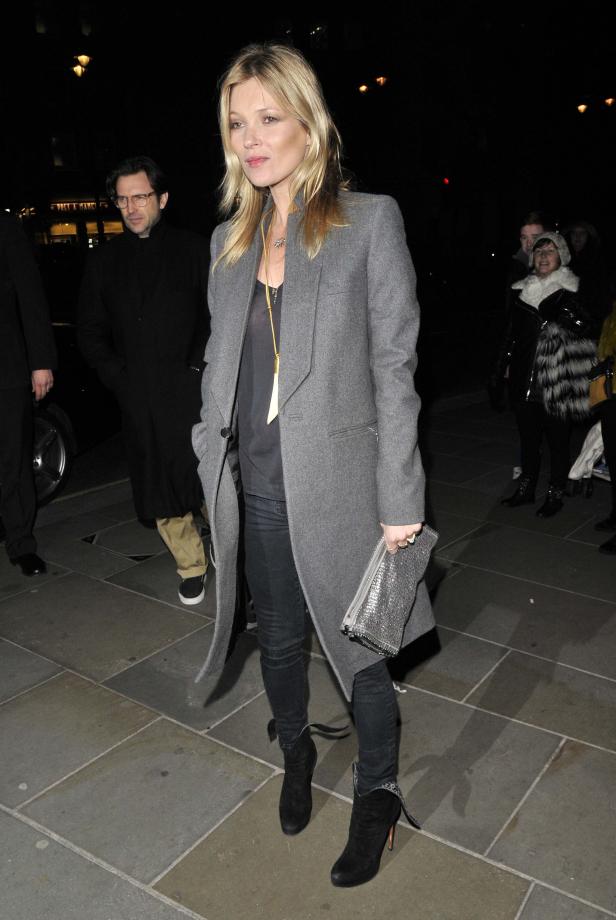 Kate Moss trägt einen grauen Mantel, dunkle Jeans und Stiefeletten.