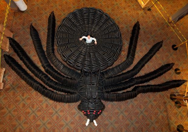 Ein Mann liegt in der Mitte einer riesigen, aus Reifen gefertigten Spinne.