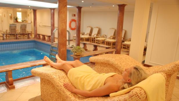 Eine Frau entspannt sich in einem Bademantel auf einer Liege am Pool.
