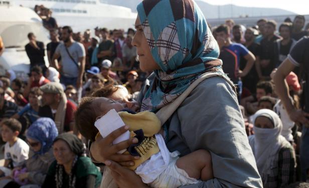 Eine Frau mit Kopftuch hält ein schlafendes Baby in einer Menschenmenge.