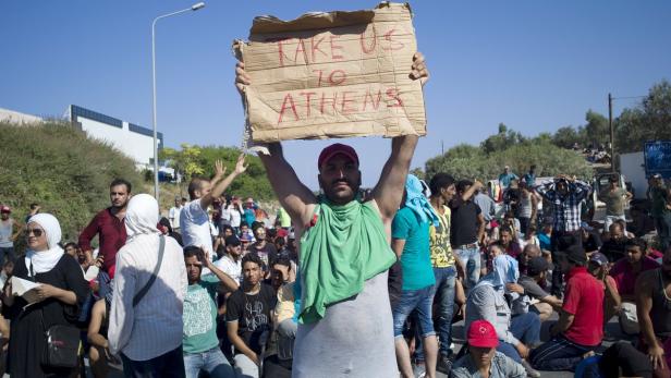 Ein Mann hält ein Schild mit der Aufschrift „Take us to Athens“ inmitten einer Menschenmenge.