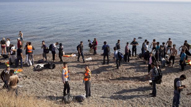 Eine Gruppe von Menschen steht am Ufer des Meeres, einige tragen Schwimmwesten.