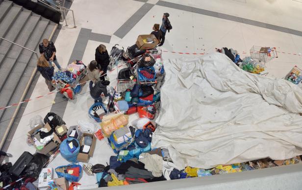 Von oben: Menschen stehen neben Spenden wie Kleidung und Hilfsgütern in Einkaufswagen und Kartons.