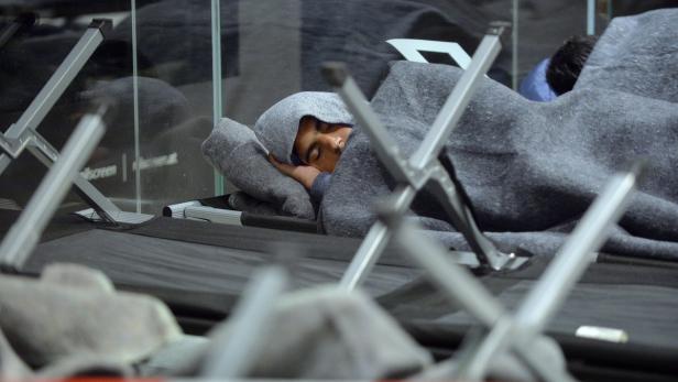 Ein Mann schläft, zugedeckt mit einer grauen Decke, auf einer Liege.