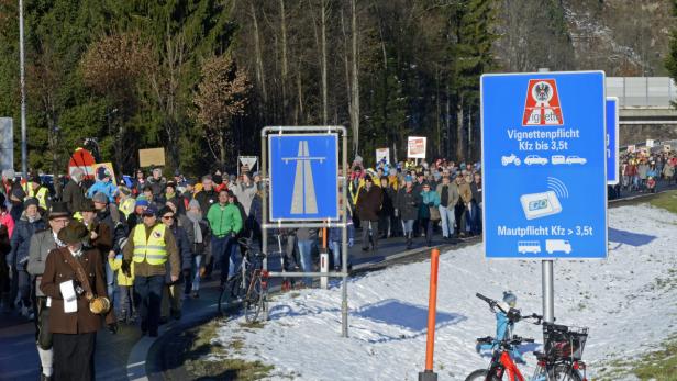Eine Menschenmenge demonstriert neben Schildern, die auf die Vignettenpflicht hinweisen.