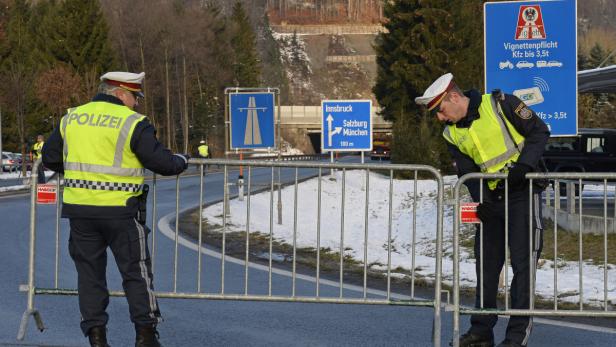 Zwei Polizisten stehen an einer Grenzkontrolle mit Hinweisschildern nach Innsbruck, Salzburg und München.
