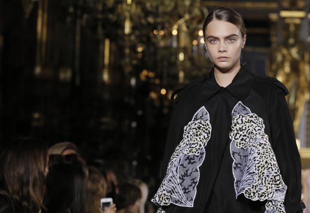 Cara Delevingne präsentiert ein schwarzes Kleid mit floralen Applikationen auf dem Laufsteg.