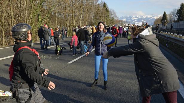 Menschen spielen Volleyball auf einer blockierten Straße vor einer Bergkulisse.