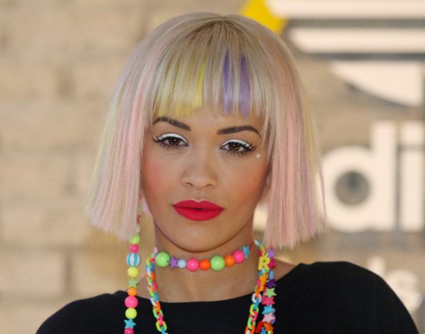 Rita Ora mit blondem Bob und bunten Strähnen, trägt farbenfrohen Schmuck.