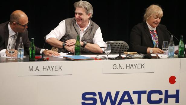M.A. Hayek, G.N. Hayek und eine weitere Person sitzen an einem Tisch mit dem Swatch-Logo.