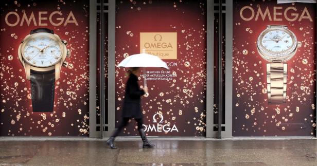 Eine Frau mit Regenschirm geht an einem Omega-Werbeplakat vorbei.