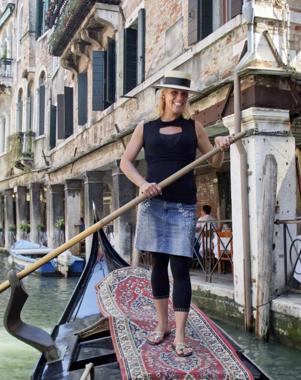 Eine Gondoliere in Venedig steht auf einer Gondel und lächelt.