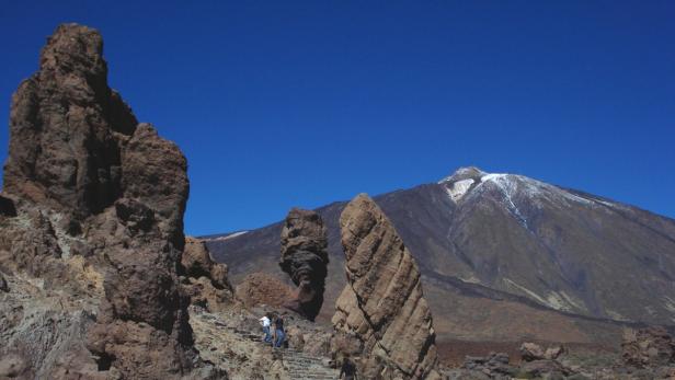 Eine Berglandschaft mit markanten Felsformationen und einem schneebedeckten Gipfel im Hintergrund.