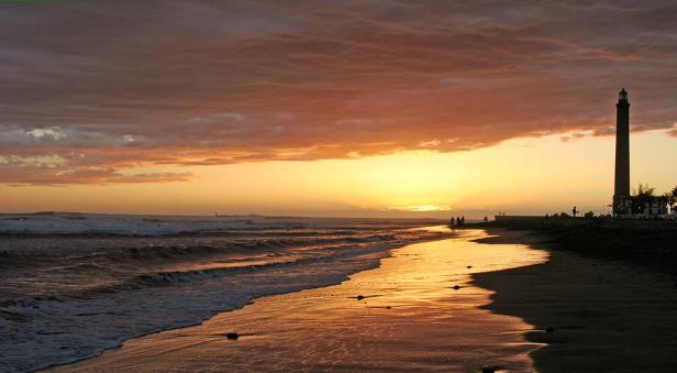 Ein Leuchtturm steht an einem Strand bei Sonnenuntergang.