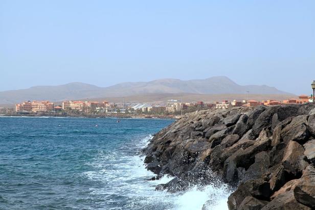 Blick auf eine Küstenstadt mit Hotels und Bergen im Hintergrund.