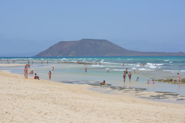 Menschen genießen den Strand mit Blick auf eine Insel.