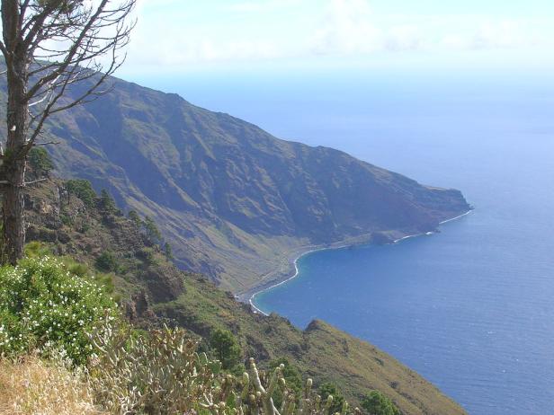 Blick auf eine grüne Küstenlandschaft mit Bergen und blauem Meer.