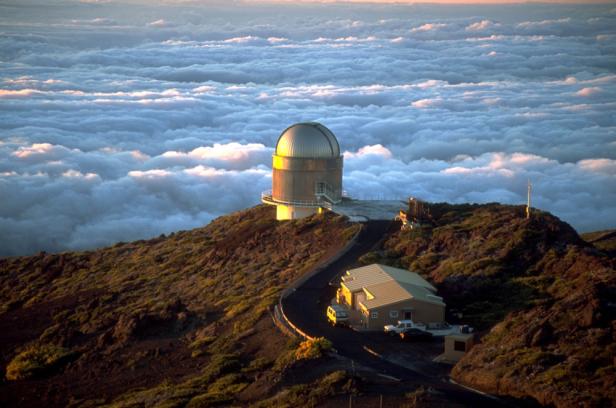 Ein Observatorium auf einem Berg mit einer Wolkendecke im Hintergrund.