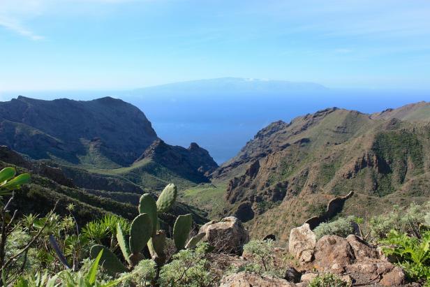 Blick durch eine grüne Schlucht auf das Meer und eine Insel am Horizont.