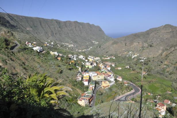Blick auf ein Dorf in einem grünen Tal mit Bergen im Hintergrund.