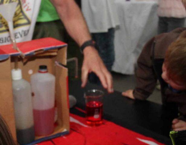 Ein Kind betrachtet ein Experiment mit Flüssigkeiten in Flaschen und einem Becher.