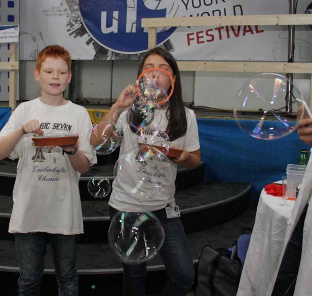 Zwei Kinder machen Seifenblasen auf einem Festival.