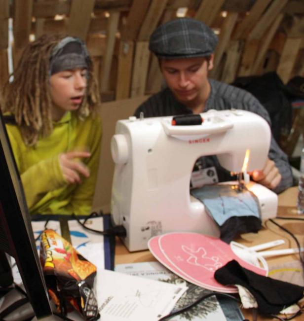 Zwei Personen sitzen an einer Nähmaschine und arbeiten an einem Projekt.