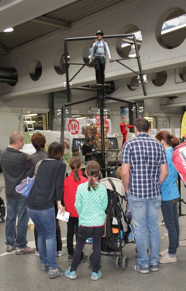 Eine Gruppe von Menschen beobachtet eine Person auf einer hohen, schwarzen Konstruktion.