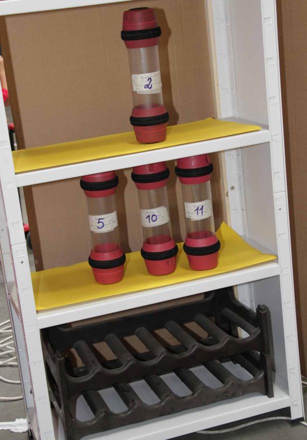 Ein Regal mit nummerierten, zylinderförmigen Behältern und einem Weinflaschenhalter.