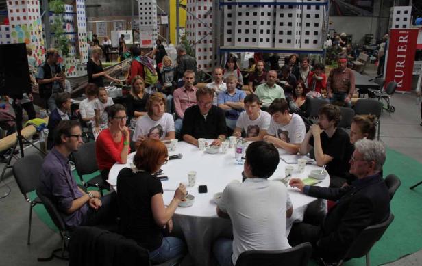 Eine Gruppe von Menschen sitzt an einem runden Tisch in einem großen Raum.