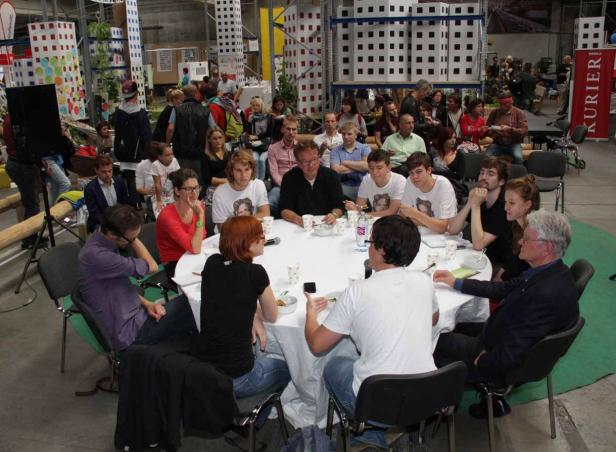 Eine Gruppe von Menschen sitzt an einem runden Tisch in einer Halle.