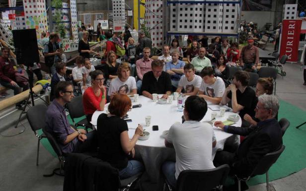 Eine Gruppe von Menschen sitzt an einem runden Tisch in einem großen Raum.