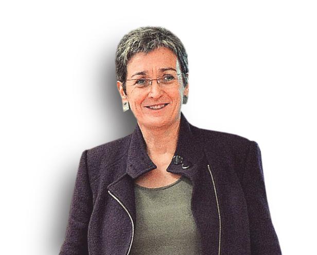 Eine lächelnde Frau mit Brille und kurzem, grauem Haar trägt ein dunkles Jackett.