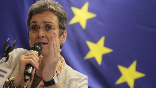 Eine Frau spricht vor einer Europaflagge in ein Mikrofon.