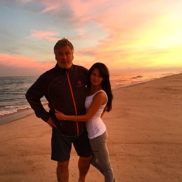 Alec Baldwin und eine Frau umarmen sich am Strand bei Sonnenuntergang.