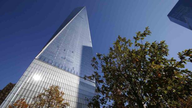 Das One World Trade Center in New York, gesehen von unten durch Bäume hindurch.