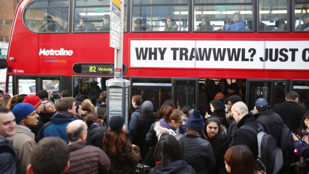 Eine Menschenmenge drängt sich an einer Bushaltestelle vor einem roten Doppeldeckerbus in London.