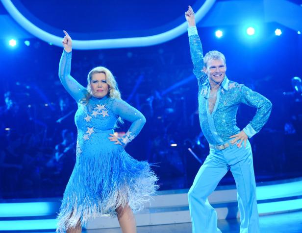 Ein Mann und eine Frau tanzen in glitzernden, blauen Kostümen auf einer Bühne.