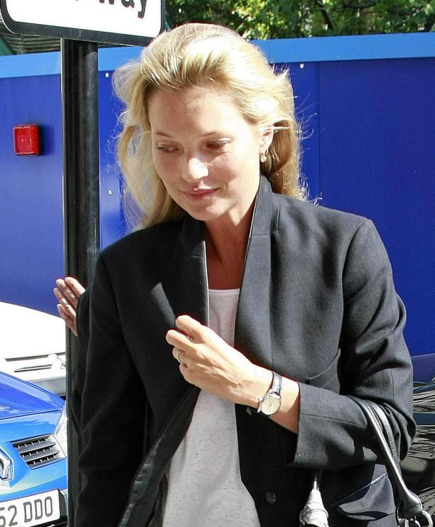 Kate Moss trägt einen schwarzen Blazer und eine Armbanduhr.