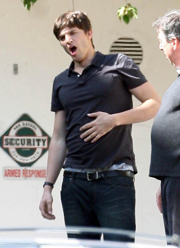 Ashton Kutcher mit schmerzverzerrtem Gesicht und Hand auf dem Bauch.