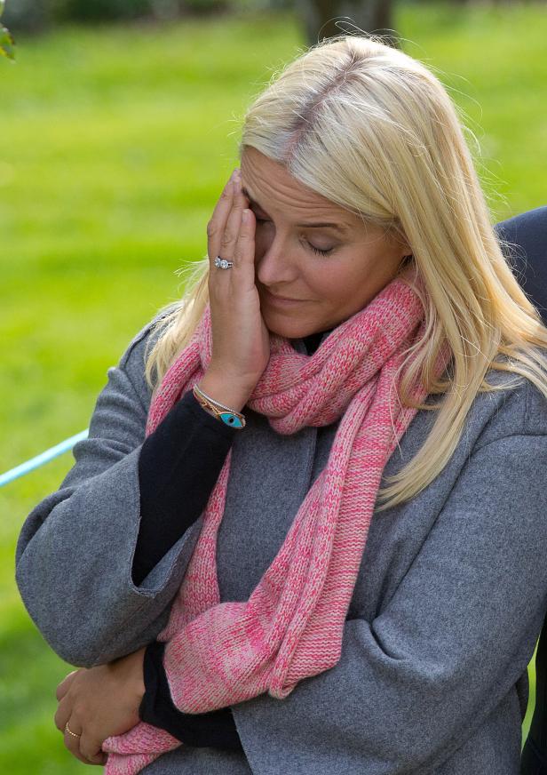 Eine blonde Frau mit einem rosa Schal weint und verdeckt ihr Gesicht mit der Hand.