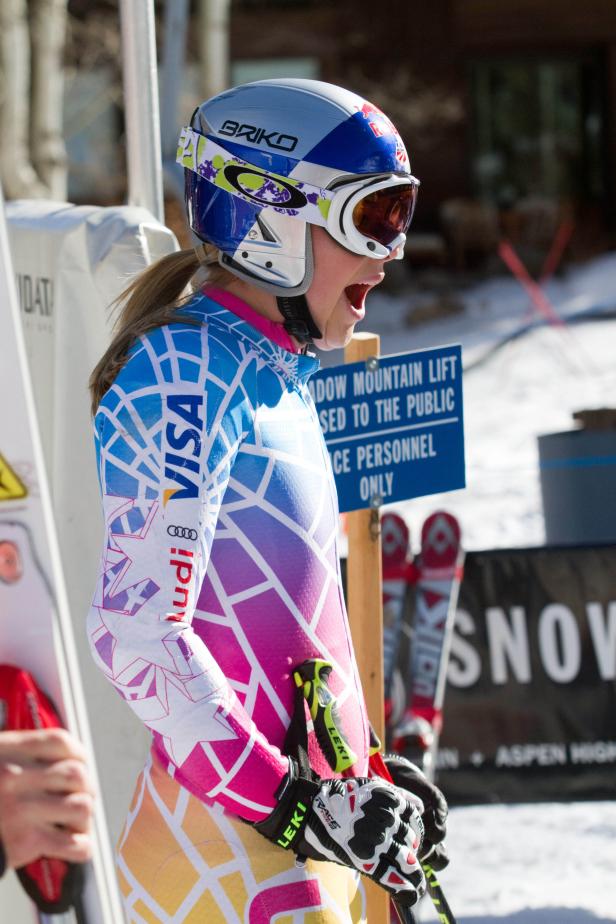 Eine Skirennläuferin mit Helm und Skianzug mit Sponsorenlogos steht am Start.