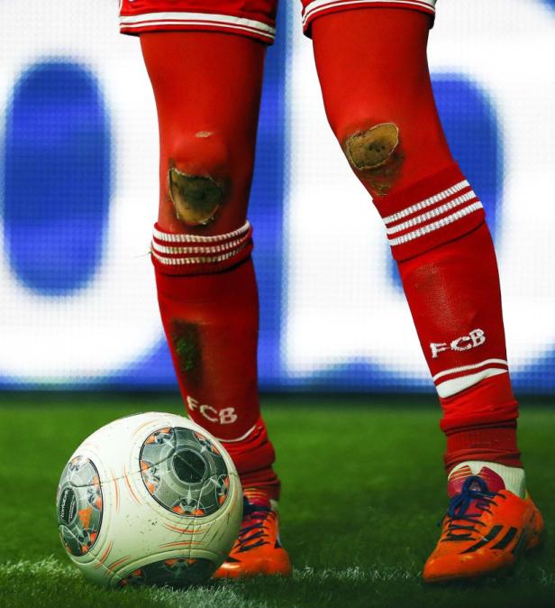 Ein Fußballspieler mit zerrissenen Stutzen und einem Fußball auf dem Rasen.