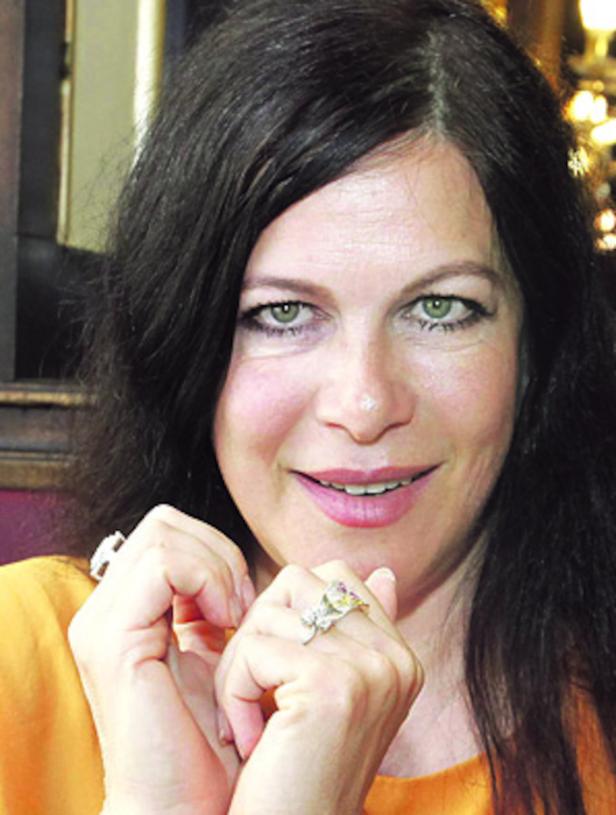 Eine Frau mit dunklen Haaren und Ringen an den Fingern lächelt in die Kamera.